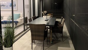 Un comedor moderno con una mesa larga y sillas de mimbre, un ventilador de techo y vista a una sala de estar con un sofá y un cuadro.