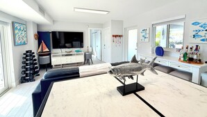 Una sala de estar moderna con un televisor de pantalla plana grande, una escultura de pez como pieza central y un comedor con una mesa de mármol.