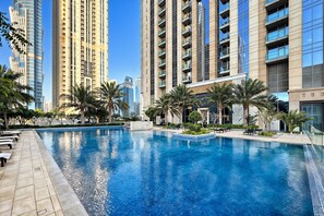 Una piscina con sillas de descanso y palmeras, rodeada de edificios altos.