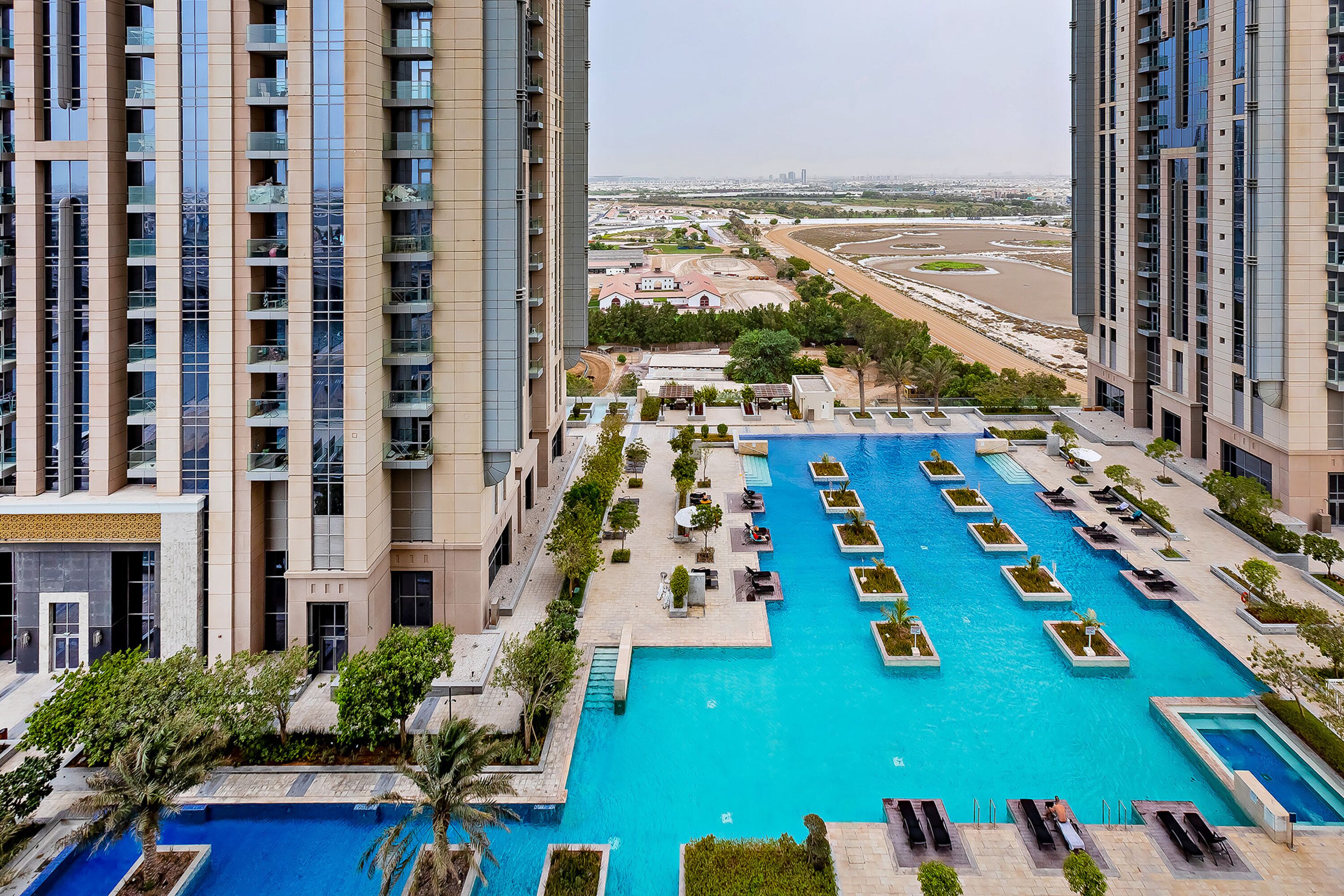 A high-rise building with a large swimming pool surrounded by lounge areas and greenery.