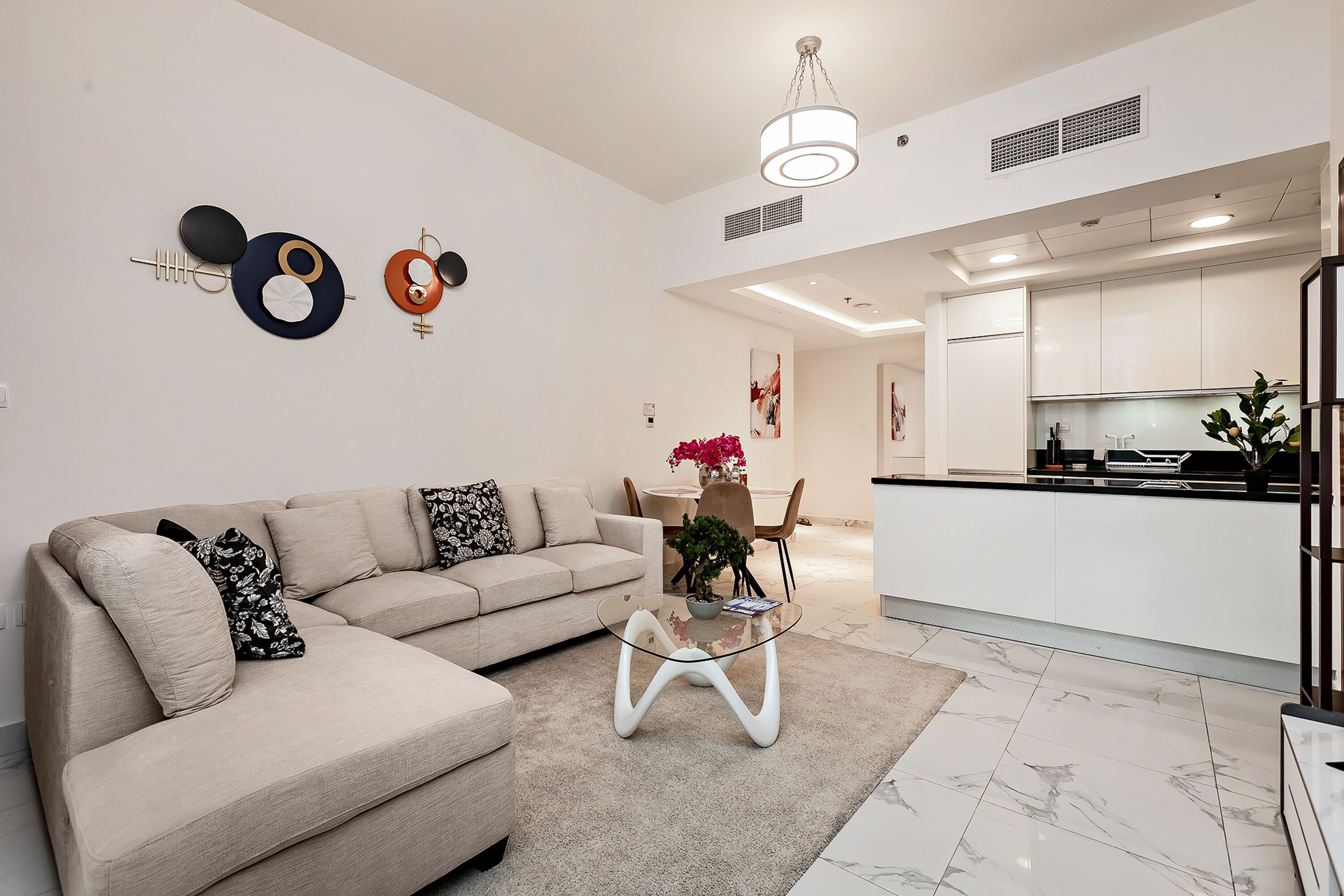 A modern living room with a beige sofa, a glass coffee table, and a kitchen in the background.