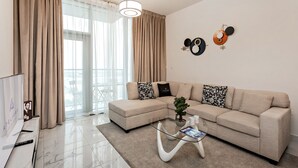 A modern living room with a beige sofa, a glass coffee table, and a TV on a stand. - Stylish 1BR Apartment at Meera Tower (Dubai)