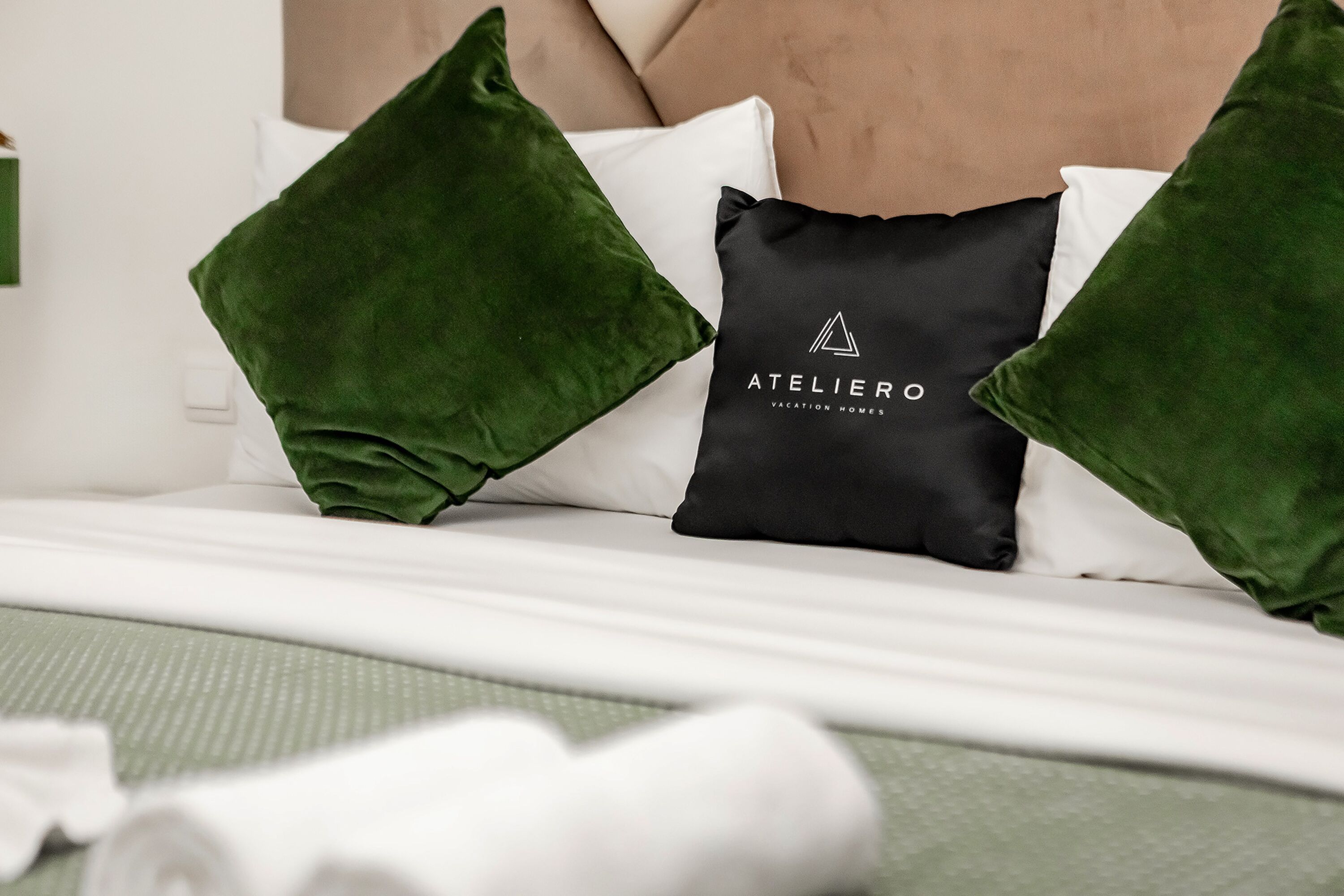 Ein ordentlich bezogenes Bett mit grünen und schwarzen Kissen, einer weißen Matratze und einer grün gemusterten Bettdecke.