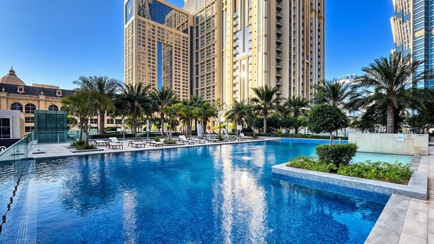 A swimming pool with lounge chairs and palm trees, surrounded by tall buildings. - Stylish 1BR Apartment at Meera Tower (Dubai)