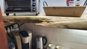 A kitchen with a toaster oven, a coffee maker, two mugs, and a bottle of Originator.