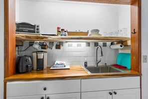 Eine kleine Küche mit einer Holzarbeitsplatte, einem Einbauofen, einer Kaffeemaschine und einem Spülbecken.