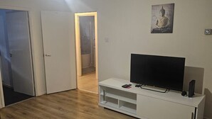 Un soggiorno con pavimento in legno, un mobile bianco con TV a schermo piatto e una porta che dà su un bagno.