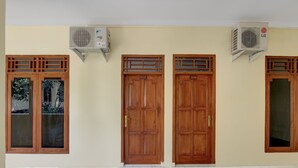 A hallway with two wooden doors, each with a number plate, and two air conditioning units mounted on the wall. - Hotel O Homestay Ka Villa Syariah (Ngrombo)