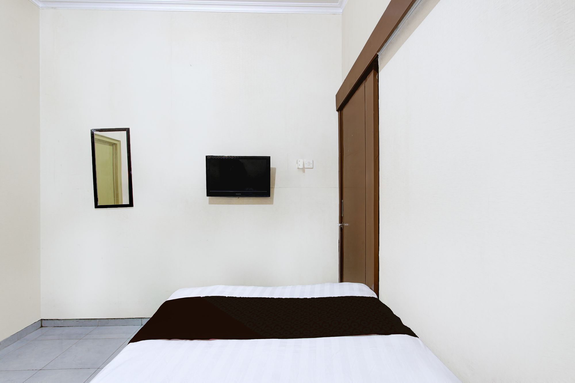A room with a bed, a television mounted on the wall, and a door.