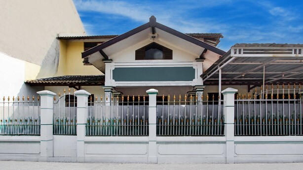A building with a white facade, a green roof, and a metal fence with decorative elements. - Hotel O Homestay Ka Villa Syariah (Ngrombo)