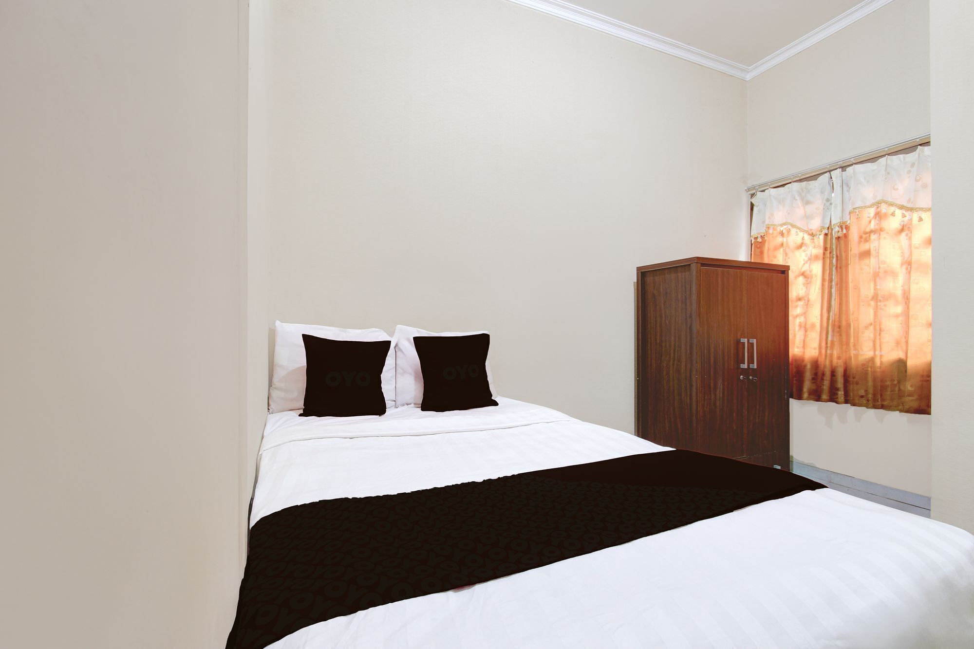 Un dormitorio con cama, dos almohadas, un armario de madera y una ventana con cortinas.
