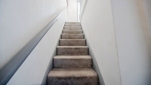 A carpeted staircase in a hallway with white walls and a handrail.