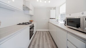 A modern kitchen with white cabinetry, a wooden countertop, a built-in oven, a microwave, and a hanging light fixture.