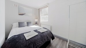 A bedroom with a bed, a window, a radiator, and a whiteboard on the wall.