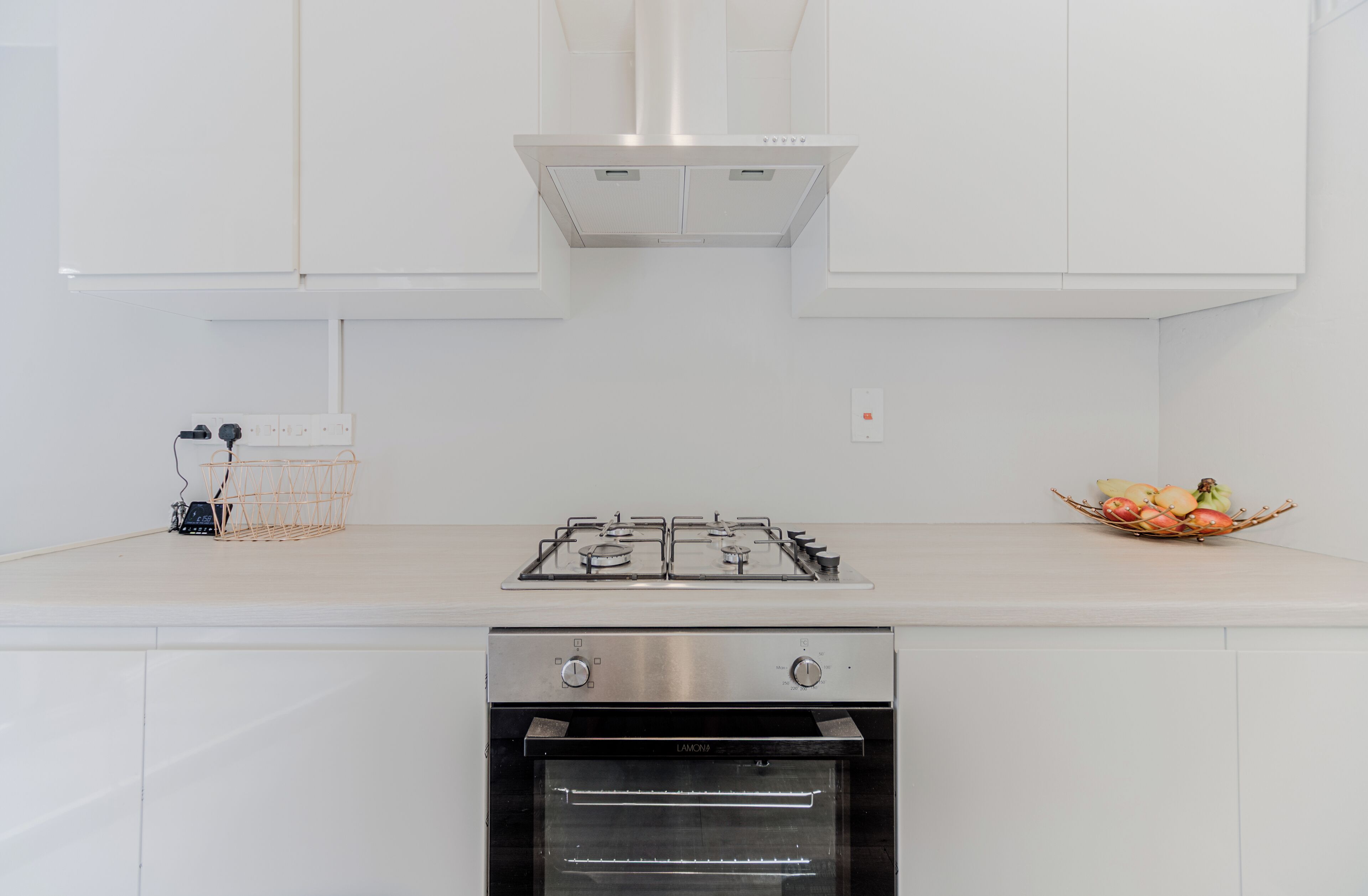 Una cucina moderna con mobili bianchi, un piano cottura a gas, un forno e una cesta di frutta sul bancone.