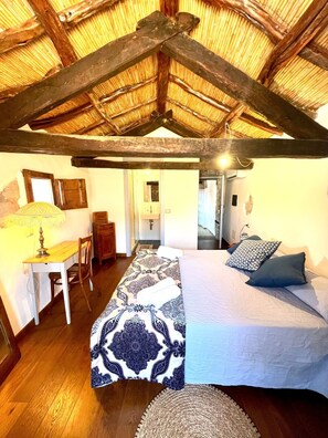 Ein Zimmer mit Bett, Schreibtisch und Stuhl. Die Decke ist aus Holz und an einer Wand befindet sich ein Fenster.