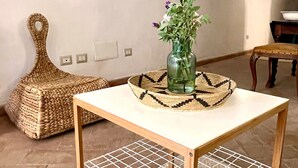 A cozy room with a woven pouf, a small table with a vase of flowers, and a stone wall. - Antico Sogno (Bosa)
