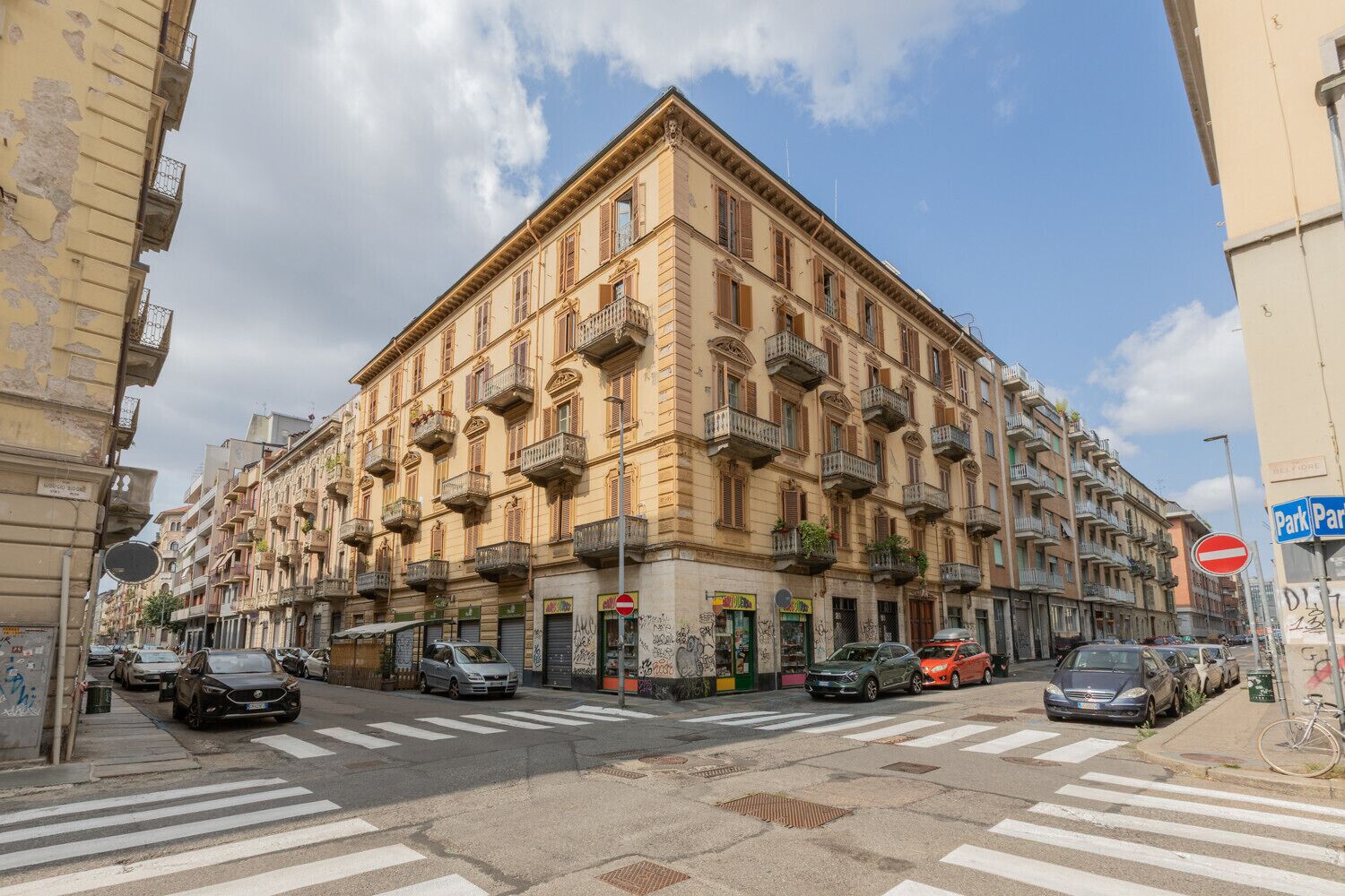 A multi-story building with balconies, a crosswalk, and parked cars.