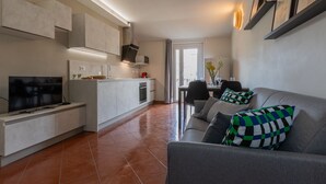 Una cocina moderna con horno empotrado, una zona de comedor con mesa y sillas, y un sofá gris con cojines estampados.