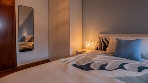 Una habitación de hotel con cama, mesita de noche, lámpara, espejo y armario.