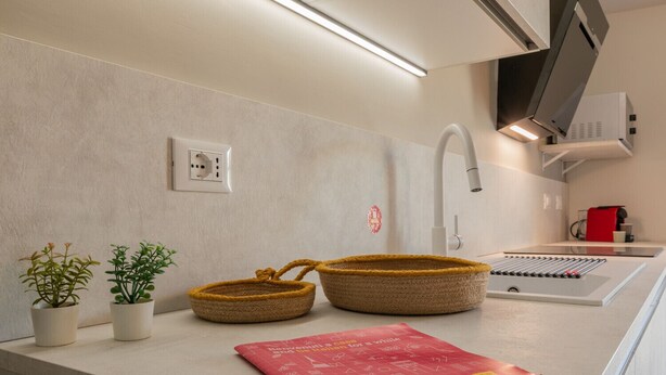 Una cocina con diseño moderno, que cuenta con una estufa integrada, un microondas y una cafetera. Hay dos macetas con plantas en la encimera.