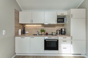 A modern kitchen with white cabinets, a built-in microwave, a coffee maker, and a dishwasher. - Holiday Home 'Nordlicht' with Private Terrace, Garden and Wi-Fi (Fehmarn)