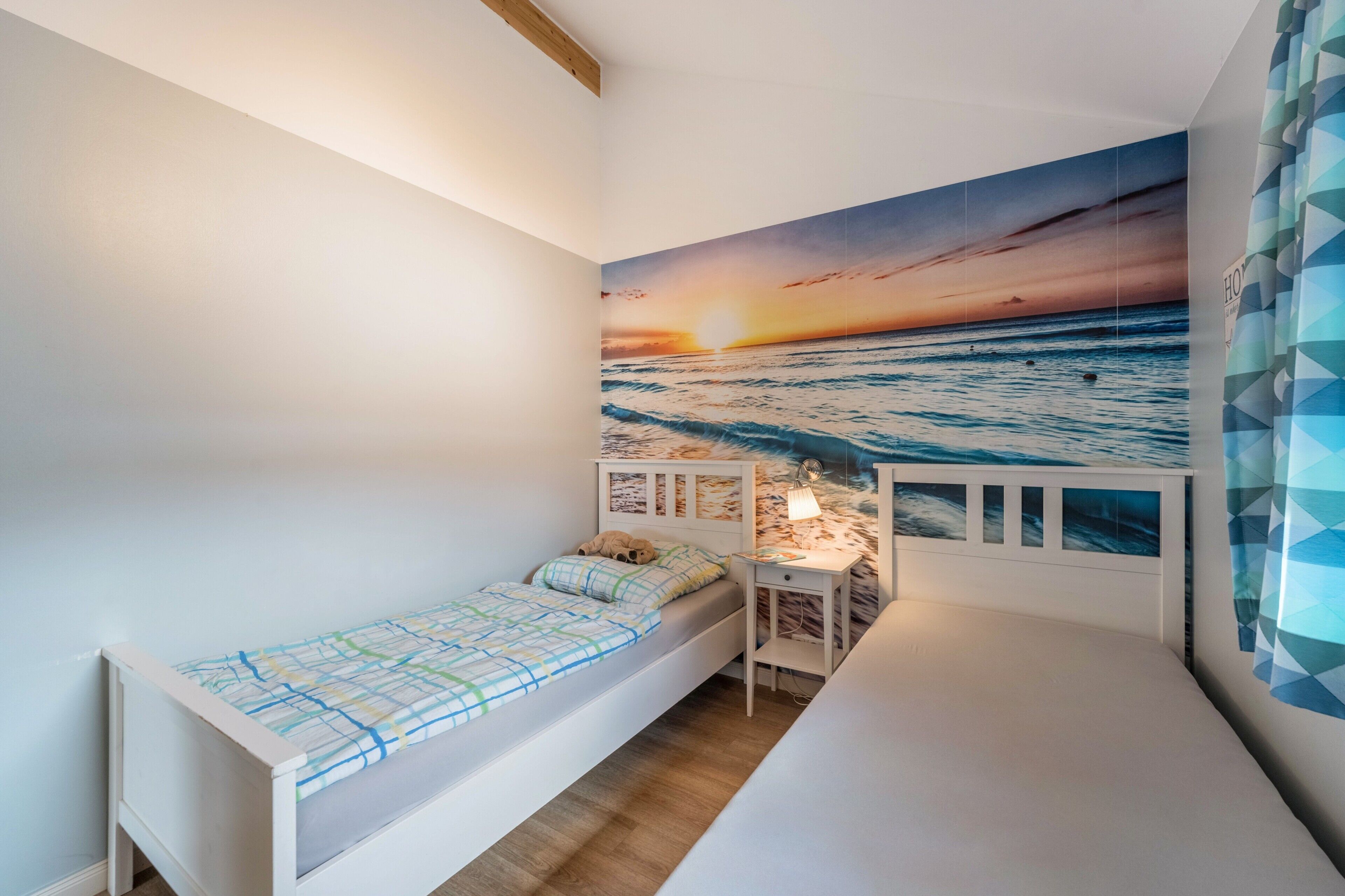 Een kinderkamer met een bed, een bureau en een muurschildering van een zonsondergang boven de oceaan.