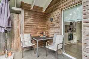 Une cabane en bois avec une table et des chaises, une petite table ornée d’une plante et une porte-fenêtre coulissante donnant sur une cuisine.