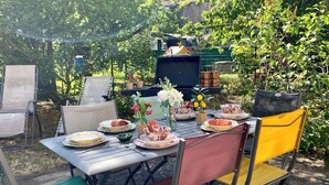 An outdoor dining area with a table set for a meal, surrounded by chairs, and a grill in the background. - New / Oasis in the Heart of Nancy with Garden and Free Parking 🍃 (Nancy)