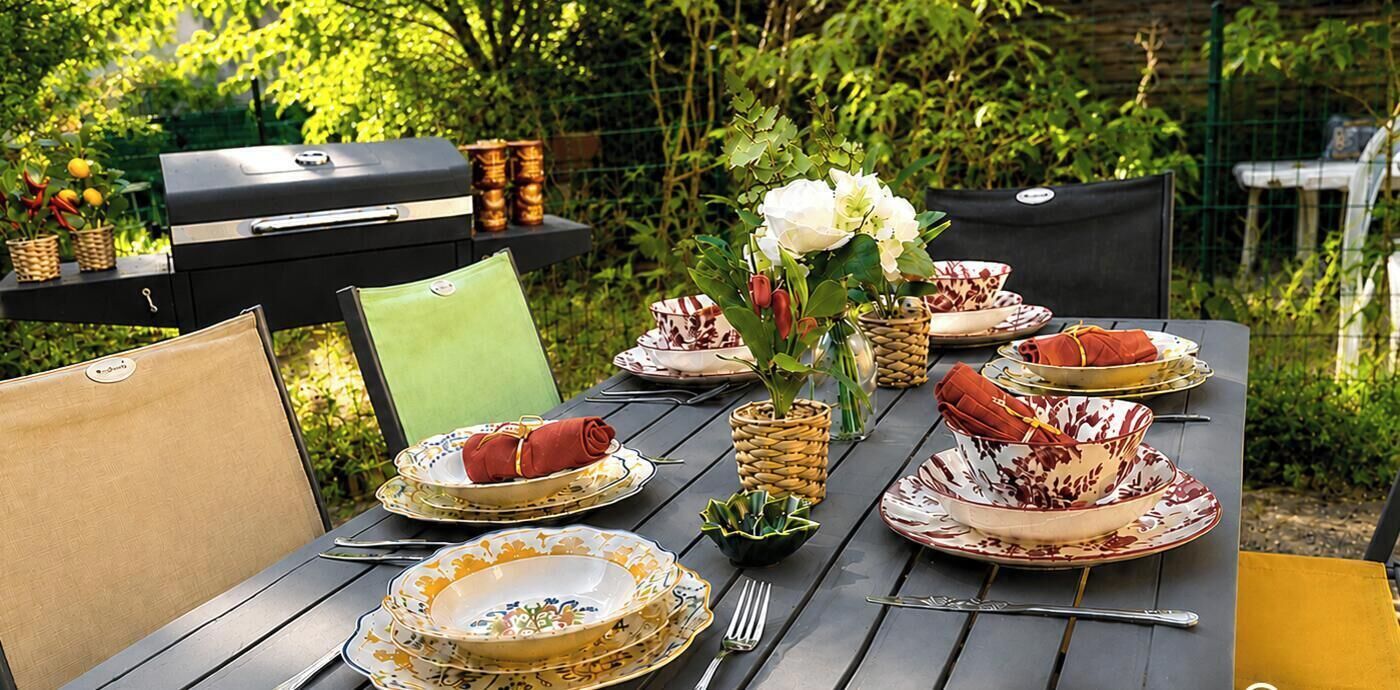 An outdoor dining table set with plates, cutlery, and a grill.