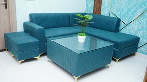 Un canapé d’angle turquoise, une table basse en verre et un pouf assorti, une plante en pot blanche et une porte en bois.