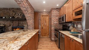 A kitchen with a stone fireplace, wooden cabinets, and modern appliances.