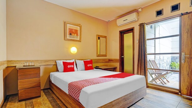 A hotel room with a wooden bed, a nightstand, a mirror, and a sliding glass door to a balcony. - Hotel O Guest House Cigadung 9a (Bandung)