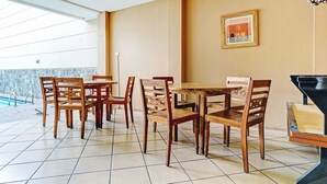 A dining area with wooden chairs and a table, a framed picture on the wall, and a pool in the background. - Hotel O Guest House Cigadung 9a (Bandung)