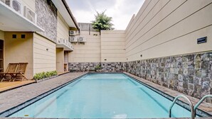 A swimming pool with stone tiles, surrounded by a building with a stone facade and a small garden area. - Hotel O Guest House Cigadung 9a (Bandung)
