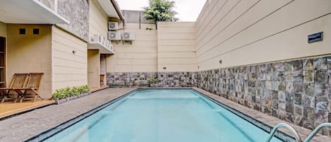 A swimming pool with stone tiles, surrounded by a building with a stone facade and a small garden area.