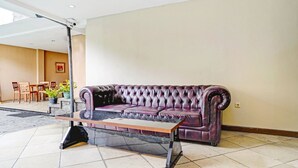 A living room with a dark purple leather sofa, a glass-top coffee table, and a dining area with wooden chairs and a table. - Hotel O Guest House Cigadung 9a (Bandung)