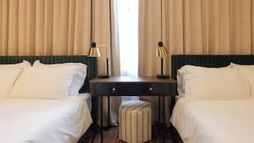 A hotel room with two beds, a desk, two lamps, and a striped ottoman.