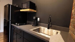 A compact kitchen with a black refrigerator, a microwave, a coffee maker, and a stainless steel sink. - Stylish 2-Bed Downtown Loft (Toledo)
