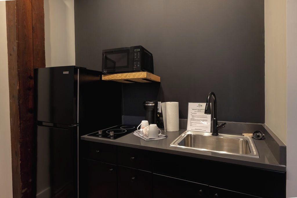 A compact kitchen with a black refrigerator, a microwave, a stainless steel sink, and a coffee maker.