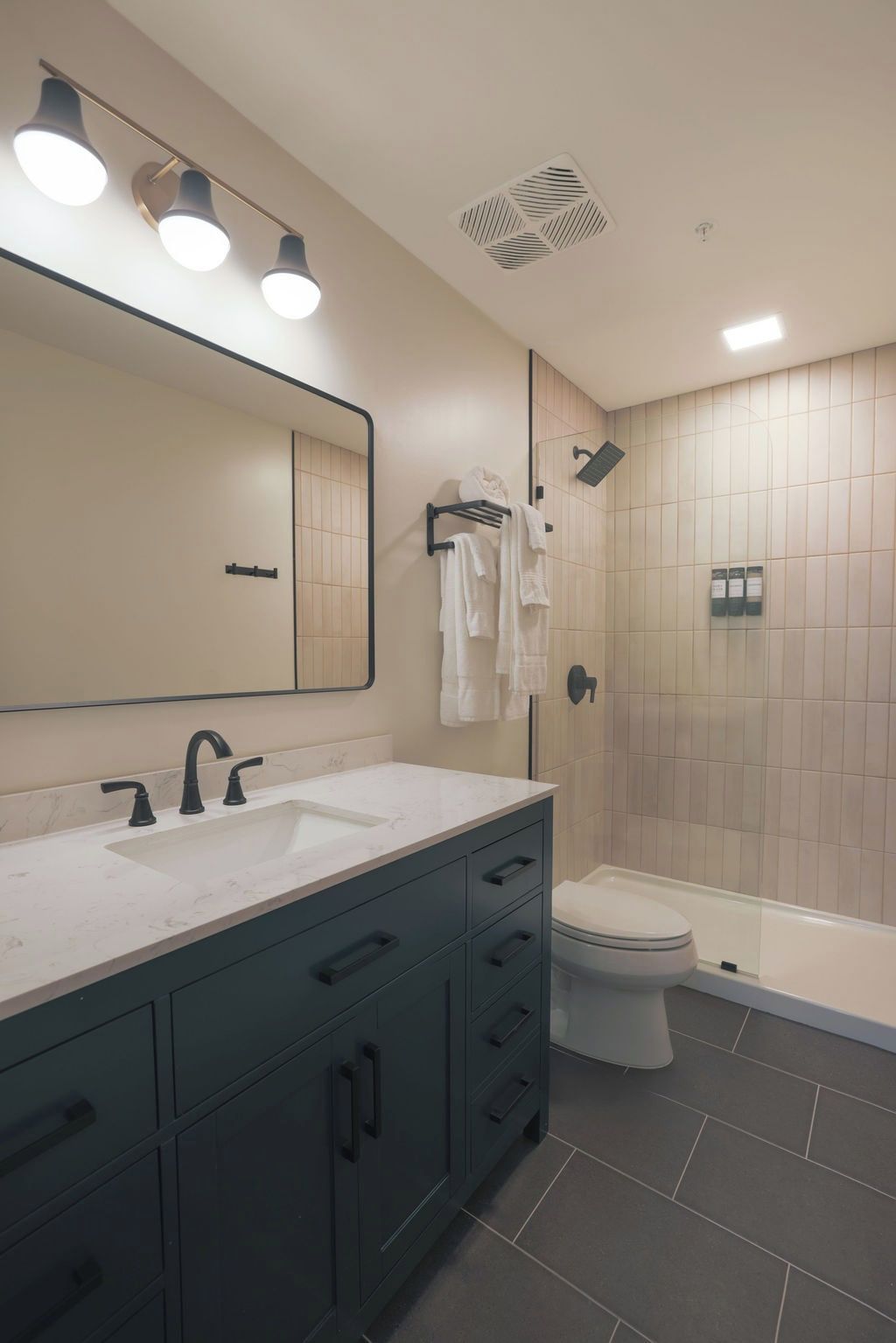 Un baño moderno con un espejo grande, un lavamanos, un inodoro y una zona de ducha.