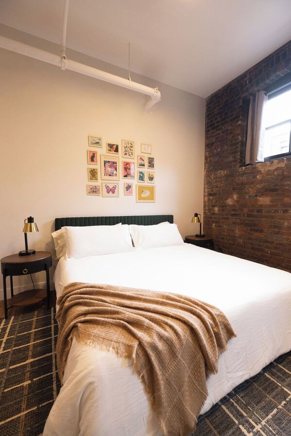Una habitación de hotel con una cama grande, una pared de ladrillo y varias fotografías enmarcadas.
