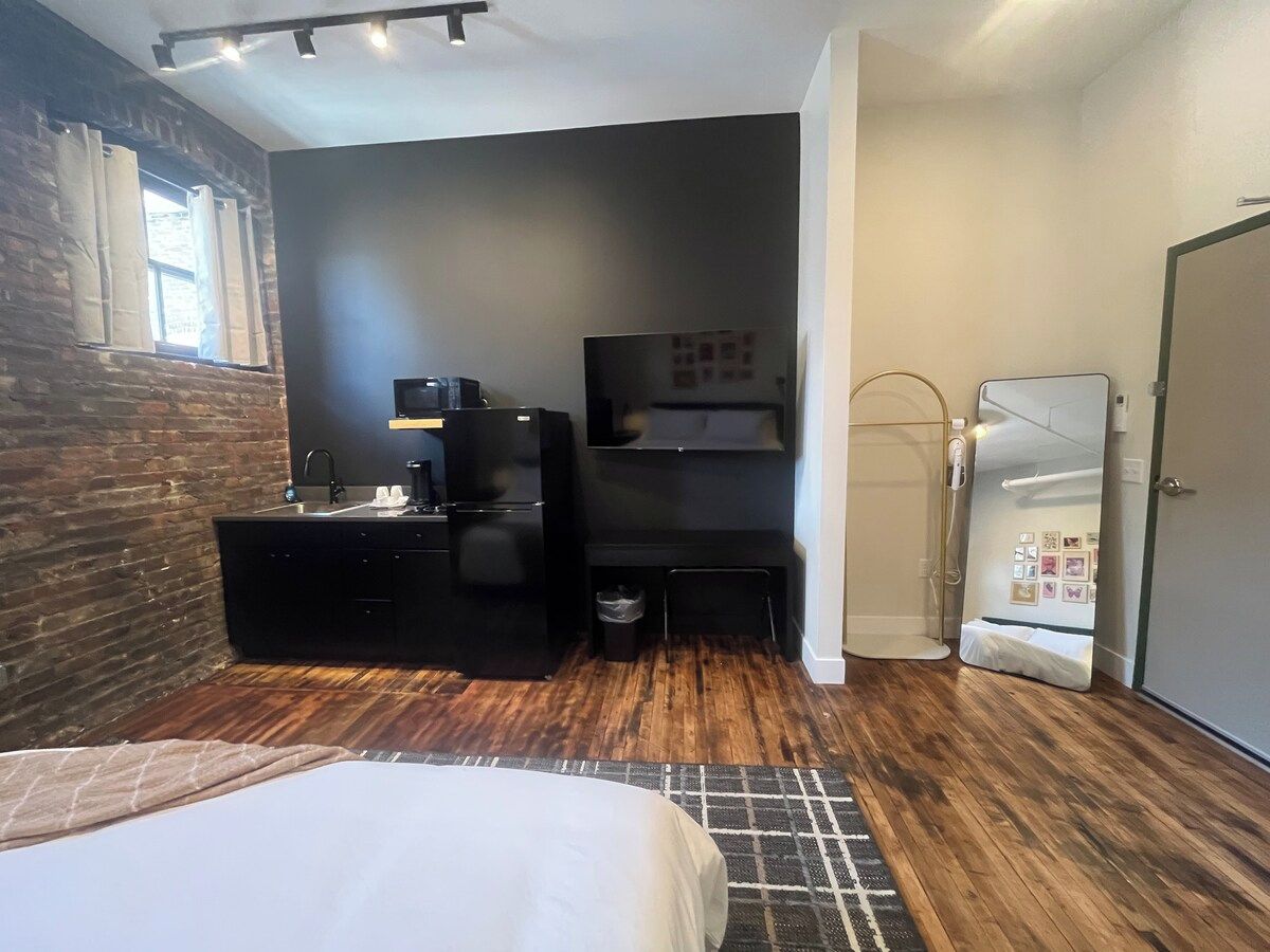 A modern hotel room with a bed, a desk, a mirror, and a wardrobe.