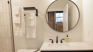 A bathroom with a white toilet, a dark blue vanity with a round mirror, and a white sink. - Downtown Loft at 5/3 Field! (Toledo)