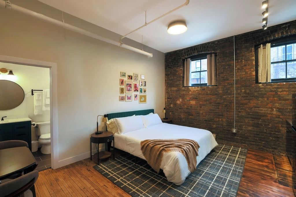 A bedroom with a bed, a nightstand, a chair, a dresser, a mirror, and a window.