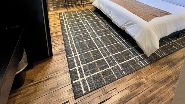 A bedroom with a brick wall, a bed with white bedding, a black TV stand, and a patterned rug. - Toledo King Loft | Ballpark & Dining | Suite 203 (Toledo)