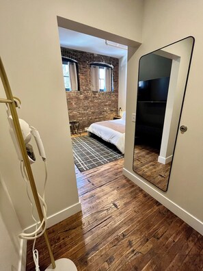 A bedroom with a large mirror, a bed, a brick wall, and a wooden floor. - Luxury Loft - Best Downtown Location (Toledo)