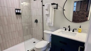 A modern bathroom with a glass shower enclosure, a toilet, a sink with a mirror, and dark-toned cabinets.