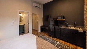 A compact hotel room with a bed, a kitchenette, a bathroom with a mirror, and a small sitting area. - Toledo King Loft | Ballpark & Dining | Suite 203 (Toledo)