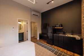 A compact hotel room with a bed, a kitchenette, a bathroom with a mirror, and a small sitting area. - Luxury Loft - Best Downtown Location (Toledo)
